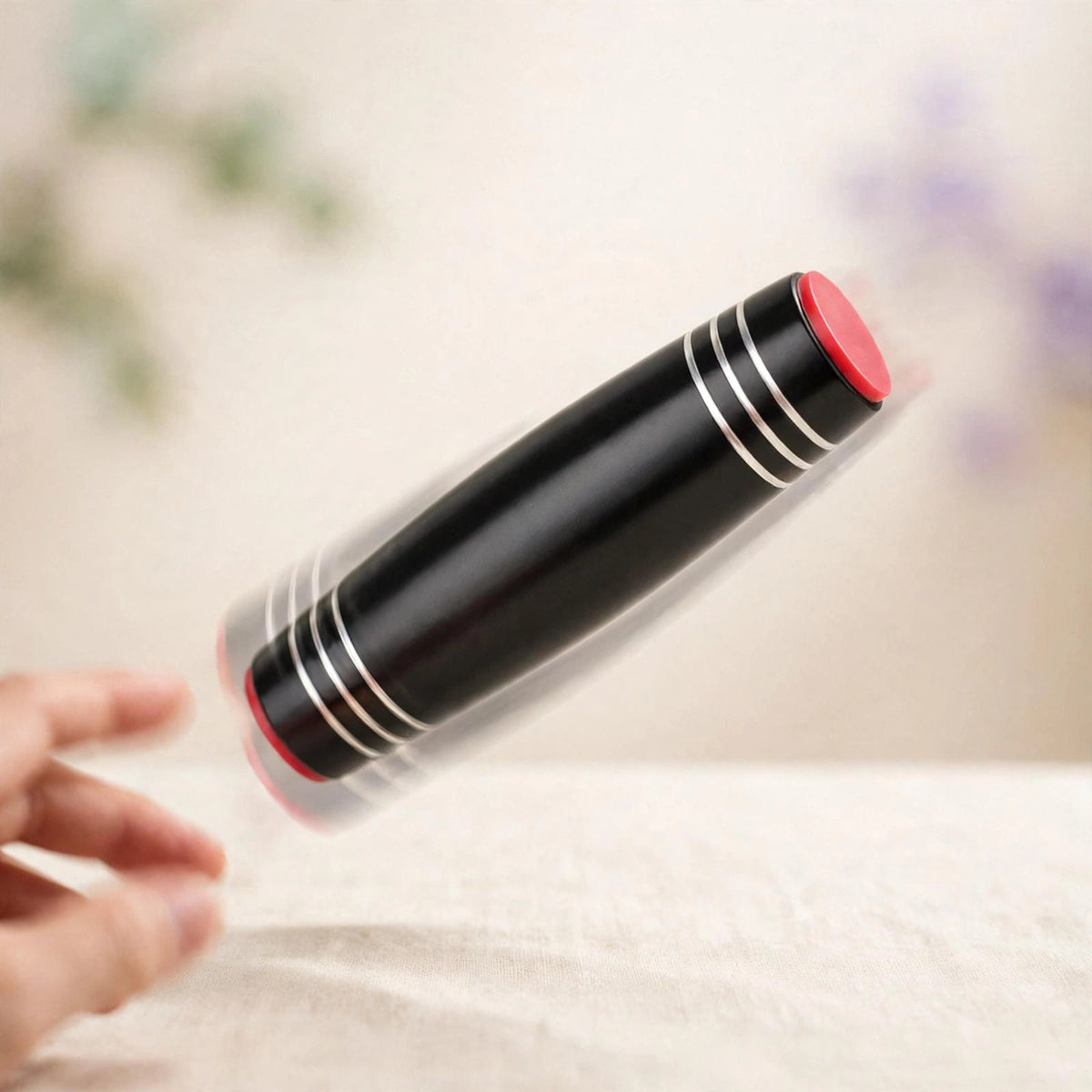 Flip Stick — black metal flip stick with red end caps tumbling mid-flip over a desk