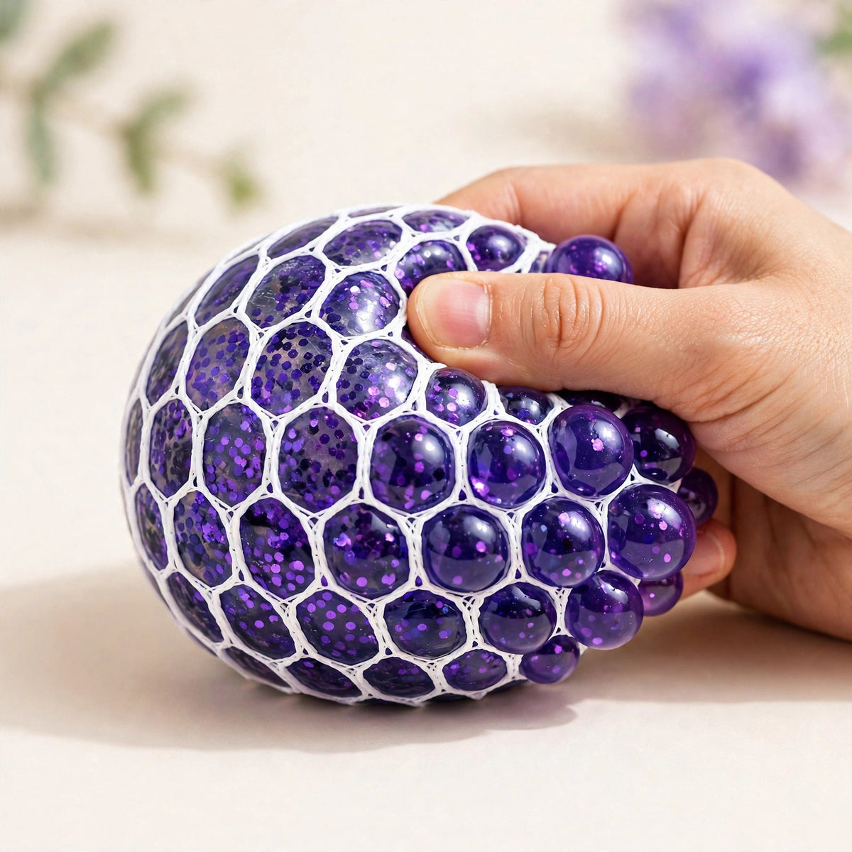 Grape Pop Ball — purple mesh squeeze ball with gel beads bulging through the net as a hand squeezes it