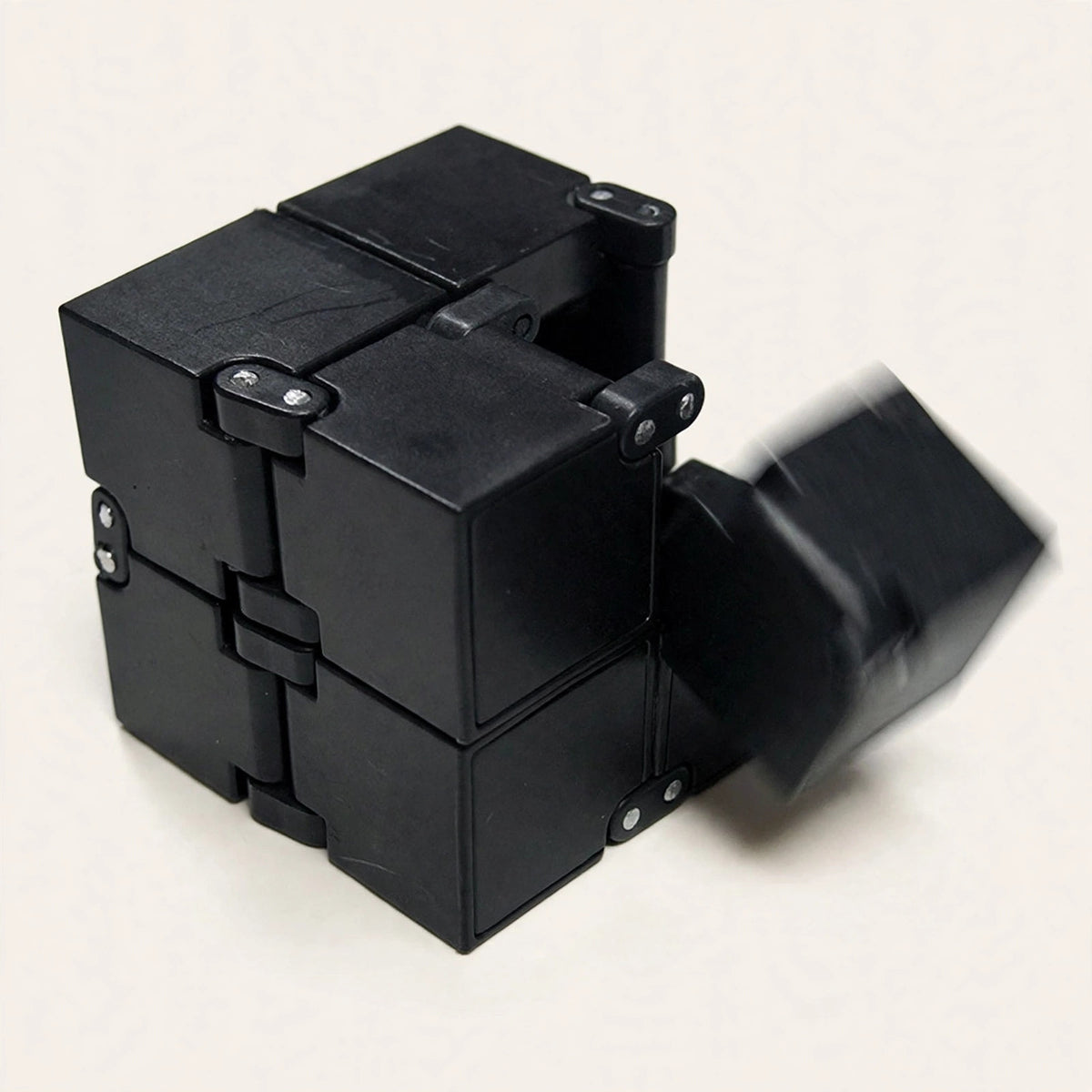 Infinity Cube — black fidget cube mid-flip on a cream background